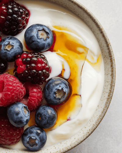Bowl of yogurt topped with berries and honey on a light surface. Bowl of yogurt topped with berries and honey on a light surface.