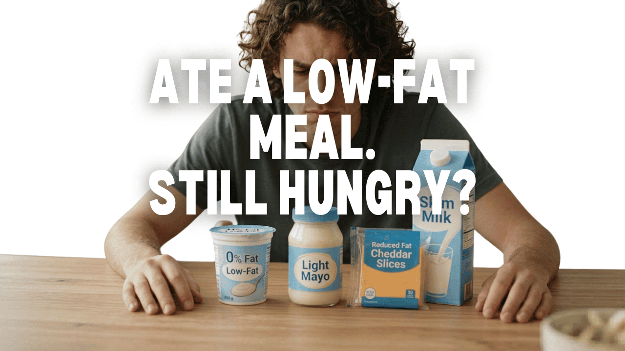 Person sitting behind low-fat foods including yogurt, light mayo, reduced-fat cheese, and skim milk with the text "Ate A Low-Fat Meal. Still Hungry?" overlayed on the image.