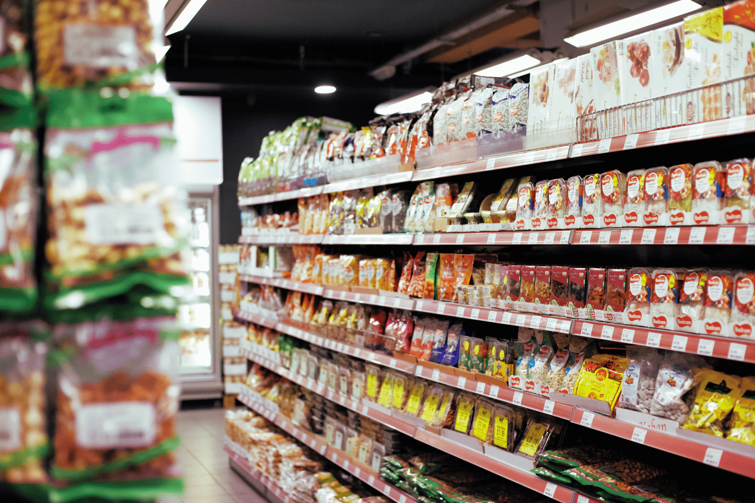 Grocery store aisle lined with packaged food products on multiple shelves under bright lighting. Grocery store aisle lined with packaged food products on multiple shelves under bright lighting.
